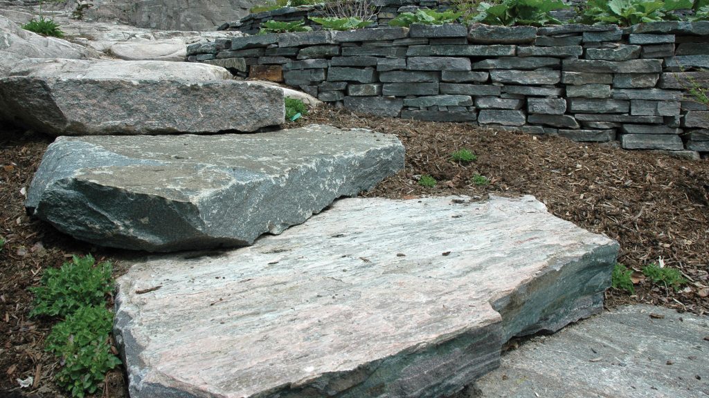 Solid stone steps in front of mulch and decorative stone wall