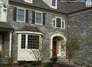 Large gray stone home with white trim and brown roof