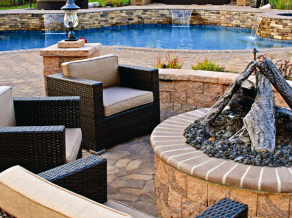 Outdoor patio with chairs and stone firepit overlooking pool with stone water features