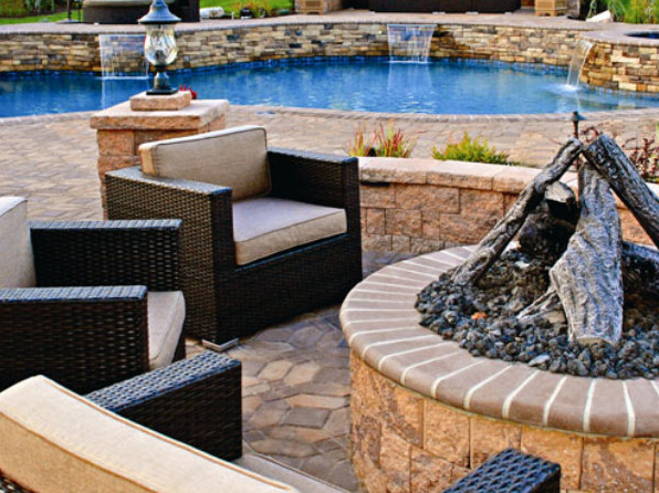 Outdoor patio with chairs and a stone firepit overlooking pool with stone water features