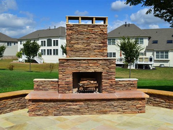 Stone paved patio and outdoor stone fireplace in front of large white home