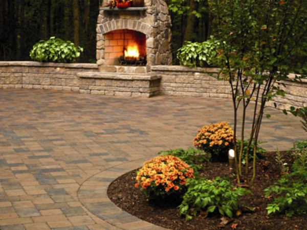 Paved patio with flowers in front of decorative stone wall and outdoor stone firplace