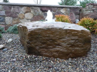 Landscape boulder on gravel in front of a decorative stone wall